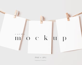 Puede incluir: Tres tarjetas blancas en blanco colgando de una cuerda con pinzas de madera. Las tarjetas están dispuestas en fila y tienen el texto "cards mockup" impreso en ellas.