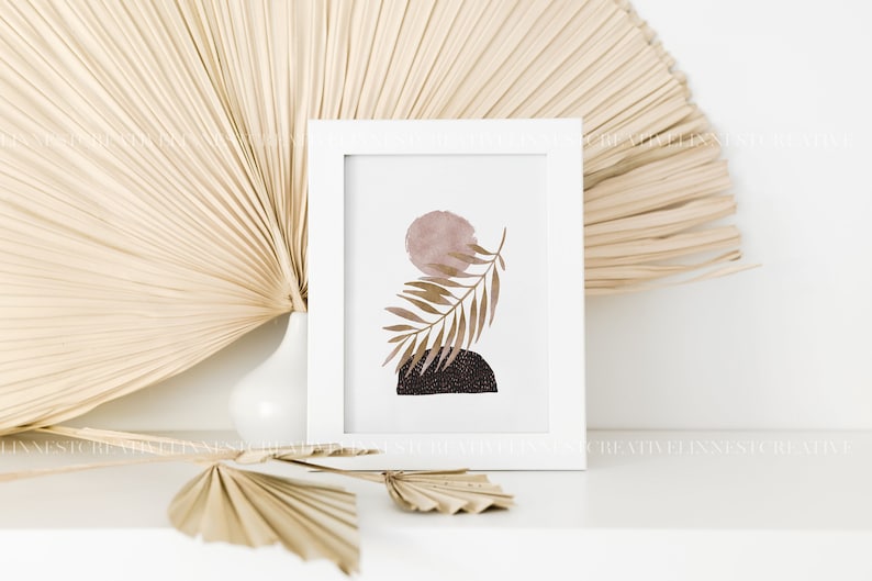 May include: A white framed print with a minimalist abstract design featuring a brown leaf, a pink circle, and a black and white geometric shape.