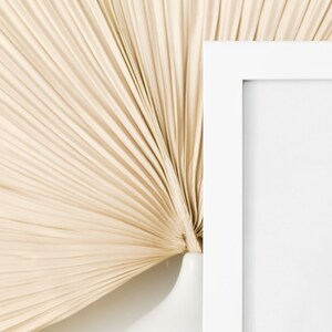 May include: A white picture frame with a white mat is positioned against a beige, fan-shaped background.