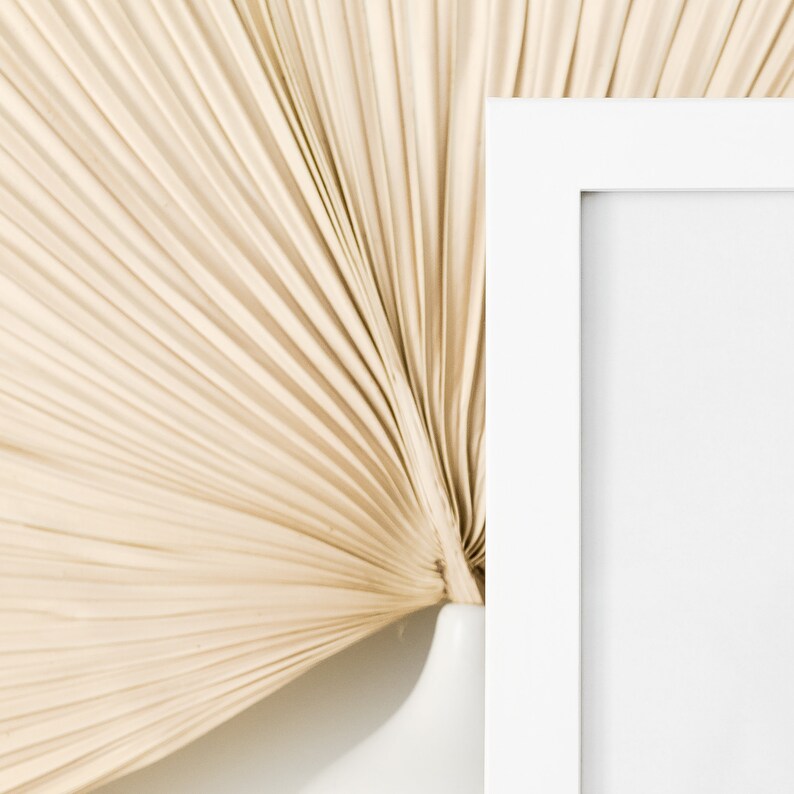 May include: A white picture frame with a white mat is positioned against a beige, fan-shaped background.
