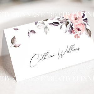 May include: A white place card with a floral design in shades of pink and gray. The name "Catherine Williams" is written in cursive on the card.