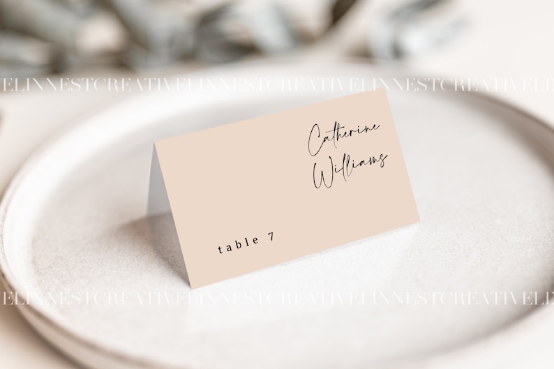 May include: A light pink table card with black text. The text reads "Catherine Williams" and "table 7".