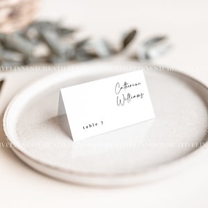 May include: White place card with black text. The text reads "Catherine Williams" and "table 7".