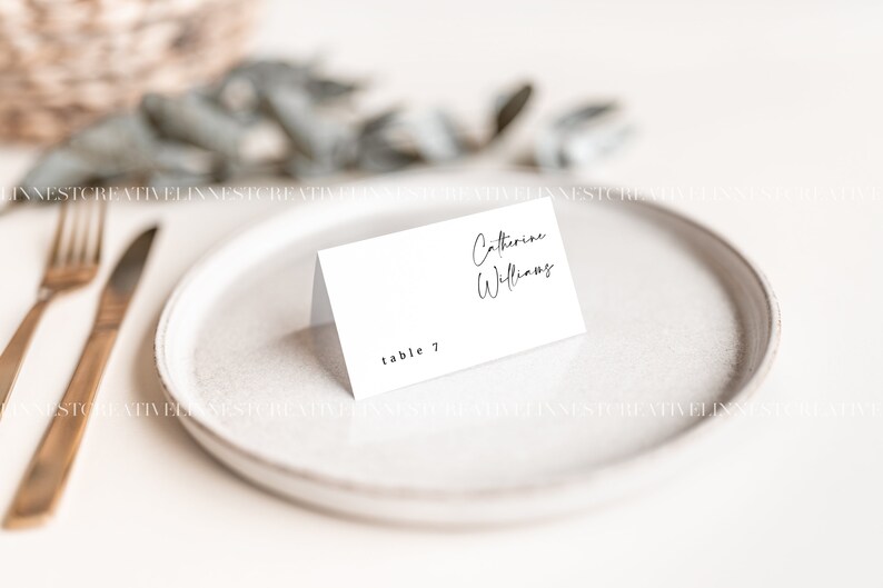 May include: White place card with black text. The text reads "Catherine Williams" and "table 7".