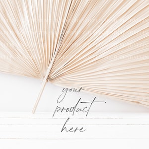 May include: A dried palm leaf fan, also known as a  'pandanus' or 'fan palm', is arranged on a white wooden surface. The text 'your product here' is written in black cursive script below the fan.