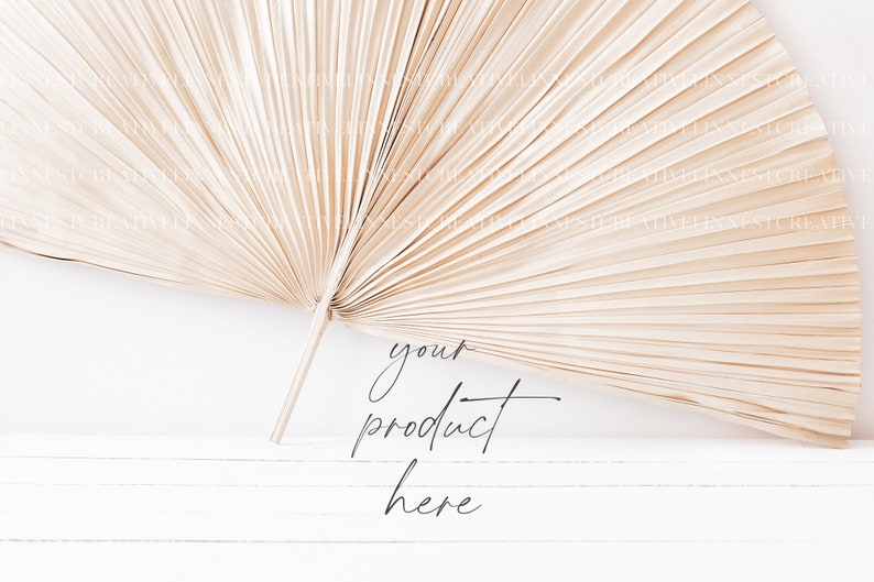 May include: A dried palm leaf fan, also known as a  'pandanus' or 'fan palm', is arranged on a white wooden surface. The text 'your product here' is written in black cursive script below the fan.