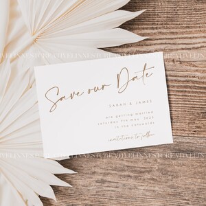 May include: A white save the date card with brown text. The text reads "Save our Date" followed by "Sarah & James are getting married Saturday 7th May 2023 in the Cotswolds. Invitations to follow."