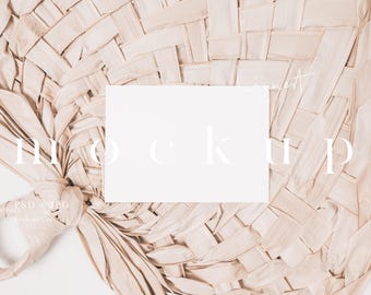 May include: A white blank card mockup on a woven natural beige background. The card is laying flat on the surface. The background is a woven material that looks like a fan.