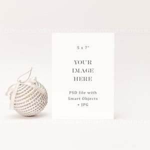 以下が含まれることがあります： 白い背景に、「5 x 7」、「YOUR IMAGE HERE」、「PSD file with Smart Objects + JPG」というテキストが書かれた白いカード。手前に白と銀のクリスマスオーナメントがある。