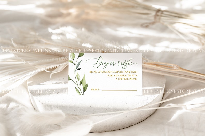 May include: A white card with green foliage and gold lettering. The card says "Diaper Raffle" and "Bring a pack of diapers (any size) for a chance to win a special prize!" There is a line for a name.