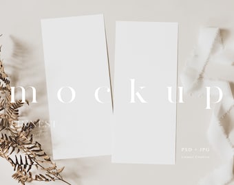 May include: Two blank white cards with a fern sprig and white ribbon on a light beige background. The text "MOCKUP" is printed in white on the cards.