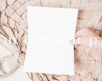 May include: A white blank sheet of paper is held by a hand against a woven background. The paper is a mockup for a design or message.