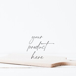 May include: A light brown wooden cutting board with a handle, sitting on a white wooden surface. The text "your product here" is written in black cursive on the board.