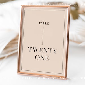 May include: A rose gold frame with a beige background and black text that reads "Table Twenty One".