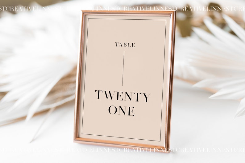 May include: A rose gold frame with a beige background and black text that reads "Table Twenty One".