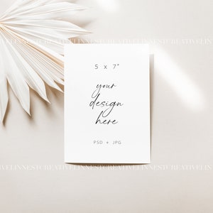 Pu&ograve; includere: Un mockup di carta bianca con il testo "5 x 7" e "your design here" su uno sfondo beige con una foglia di palma secca nell'angolo in alto a sinistra.