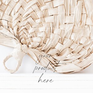 May include: A woven, beige fan with a handle. The fan is leaning against a white wall with the text "your product here" written below it.