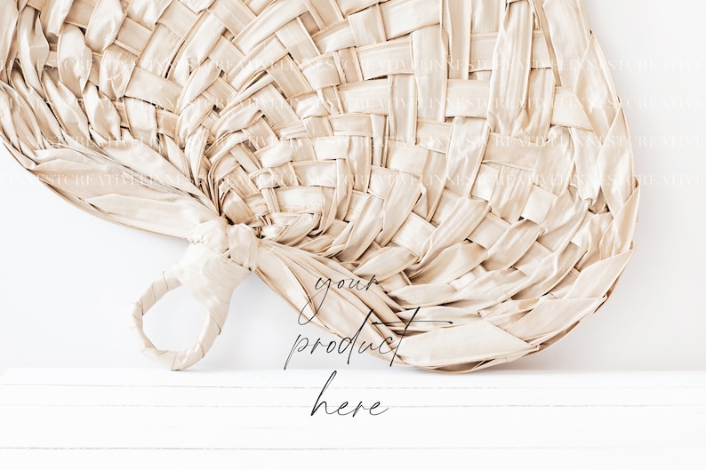 May include: A woven, beige fan with a handle. The fan is leaning against a white wall with the text "your product here" written below it.