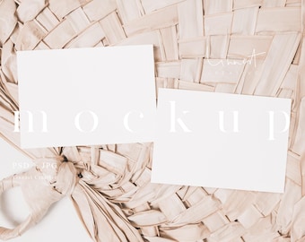 May include: Two blank white cards on a woven natural beige background. The cards are lying flat on the surface. The text "MOCKUP" is written in white on the background.