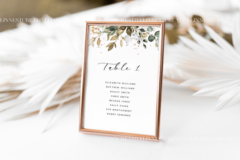 May include: A white card with a gold frame and a floral design at the top. The card says "Table 1" and lists the names of guests: Elizabeth Williams, Matthew Williams, Hailey Smith, Chris Smith, Meghan Jones, Sally Evans, Eva Montgomery, and Harry Sowards.