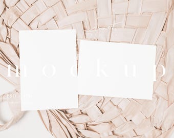 May include: Two blank white cards on a woven beige background. The cards are lying flat on the surface. The text "MOCKUP" is written in white on the background.