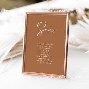May include: A rose gold framed table number card with the number "Six" written in white cursive script. The card lists the names of guests assigned to table six, including Elizabeth Williams, Matthew Williams, Mailey Smith, Chris Smith, Meghan Jones, Sally Evans, Eva Montgomery, Harry Edwards, Sandra Stevenson, and Kevin Stevenson.