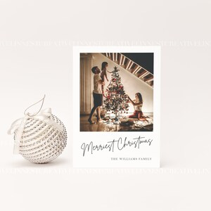 以下が含まれることがあります： クリスマスツリーを飾る家族の写真が載った白いクリスマスカード。カードには「メリエストクリスマス」と「ザ・ウィリアムズ・ファミリー」の文字が印刷されています。