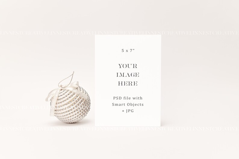 以下が含まれることがあります： 白い背景に、「5 x 7」、「YOUR IMAGE HERE」、「PSD file with Smart Objects + JPG」というテキストが書かれた白いカード。手前に白と銀のクリスマスオーナメントがある。