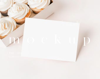 May include: A white card mockup with the word "mockup" written in white text on a white background. The card is sitting on top of a white box filled with cupcakes.