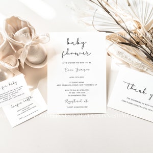 May include: A white card with black text announcing a baby shower for Cara Jameson on April 15th, 2022. The card includes the address, RSVP information, and registry details. There are also two smaller white cards with black text, one for a diaper raffle and one for a "look for baby" game.