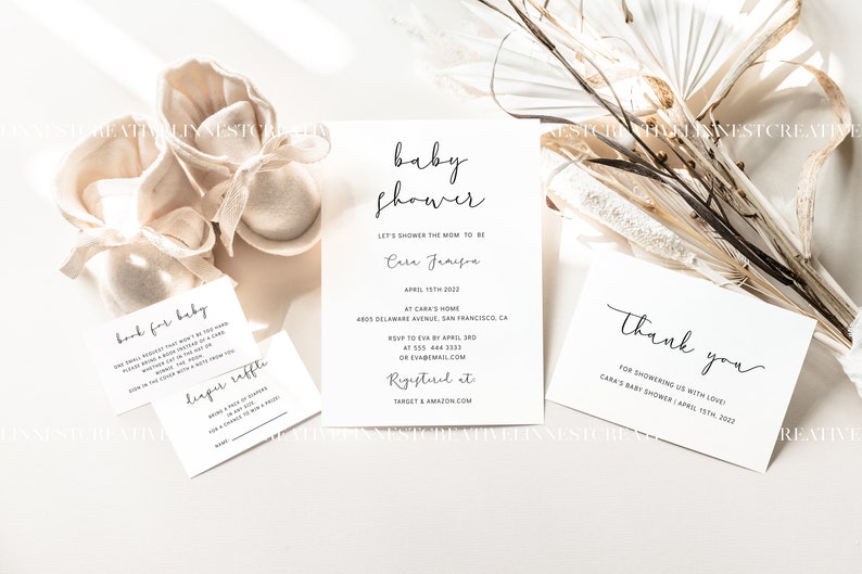 May include: A white card with black text announcing a baby shower for Cara Jameson on April 15th, 2022. The card includes the address, RSVP information, and registry details. There are also two smaller white cards with black text, one for a diaper raffle and one for a "look for baby" game.