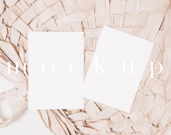May include: Two blank white rectangular cards rest on a beige woven fabric background. The word "mockup" is written in a light colour across the cards. The fabric has a textured, woven appearance, and the overall aesthetic is minimalist and neutral.