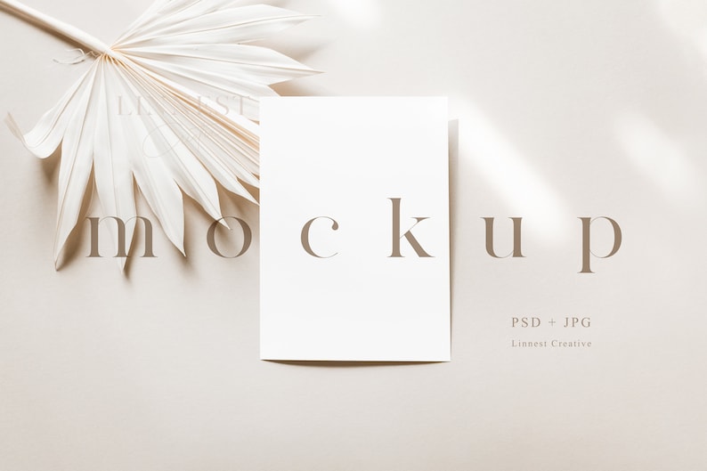 Pu&ograve; includere: Un mockup di una carta bianca con la parola "mockup" stampata in testo marrone su uno sfondo beige. Una foglia di palma secca si trova nell'angolo in alto a sinistra dell'immagine.