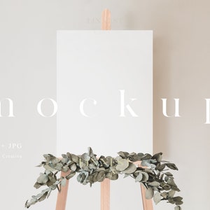 May include: A white blank canvas mockup on an easel with a garland of green eucalyptus leaves.