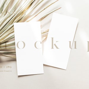 Op de afbeelding: Twee lege witte kaarten op een beige achtergrond met een gedroogd palmblad. De tekst "mockup" staat in lichtbruine letters op de kaarten.