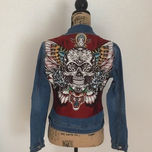 May include: A blue denim jacket with a red, white, and black skull and butterfly design on the back.