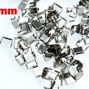 May include: A pile of silver metal 3mm zipper slider stoppers.