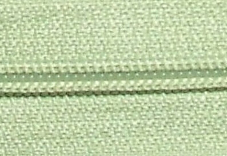 May include: A close-up of a light green zipper tape with a white zipper pull. The zipper tape has a textured surface.