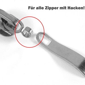 Op de afbeelding: Zilveren rits-schuifreparatieset met de tekst "Für alle Zipper mit Hacken!" wat "Voor alle ritsen met tanden!" betekent.