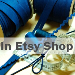 May include: Two large spools of dark blue bias tape, two small spools of dark blue thread, a length of dark blue rickrack trim, and a white measuring tape showing metric units, all arranged together for sewing and crafting projects.