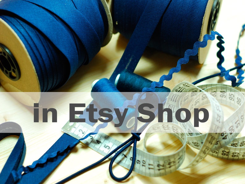 May include: Two large spools of dark blue bias tape, two small spools of dark blue thread, a length of dark blue rickrack trim, and a white measuring tape showing metric units, all arranged together for sewing and crafting projects.