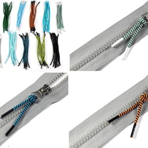 Könnte beinhalten: Nahaufnahme eines Reißverschlusses mit verschiedenen farbigen Reißverschluss-Zierbändern. Der Reißverschluss ist grau und die Bänder sind schwarz, grün, blau und orange.