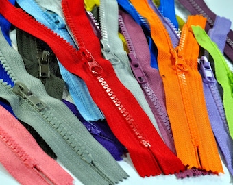 May include: A collection of plastic zippers in a variety of vibrant colors including red, orange, lime green, light blue, dark blue, purple, gray, and pink. Each zipper features a matching plastic pull tab and interlocking teeth along the tape.