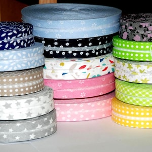 May include: A collection of fabric ribbon rolls stacked in three columns. The ribbons feature various patterns including white stars on gray, white dots on beige, floral prints on blue, black, and pink, and polka dots on bright green and yellow backgrounds.