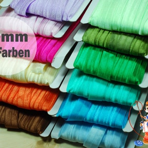 Könnte beinhalten: Ein Stapel aus 25 verschiedenen farbigen Gummibändern, jedes 20 mm breit. Das Band ist in einem Regenbogenmuster angeordnet, wobei die Farben von Helllila bis Dunkelblau reichen. Das Band wird auf weißem Karton präsentiert. Der Text "20mm 25 Farben" ist im Bild sichtbar.