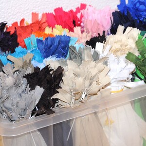 May include: A clear plastic storage container filled with a variety of colours of zips. The zips are organised by colour and are ready to be used for sewing projects.