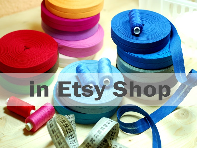 May include: Multiple rolls of colorful bias tape in red, orange, pink, light blue, and dark blue, accompanied by matching sewing thread spools and a white measuring tape with black markings showing numbers up to 150 centimeters for scale.