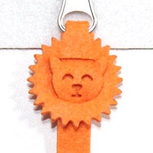 May include: Orange felt zipper pull featuring a smiling lion face with a sun-like mane. The pull is attached to a silver metal zipper. The lion's face is detailed with small, simple features.