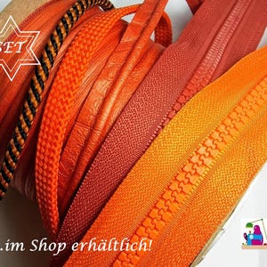 May include: A collection of various orange and reddish-orange zippers and cords wound on spools. The assortment includes textured orange cords, a black and orange patterned cord, and several smooth orange and red zipper tapes with plastic teeth.