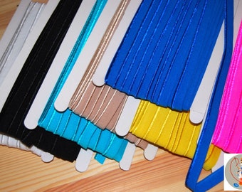 May include: A collection of colorful elastic ribbon spools in various shades, including silver, black, turquoise, tan, blue, yellow, and pink. Each ribbon is neatly displayed on a white card, showcasing its texture and color. The ribbons are arranged on a wooden surface.